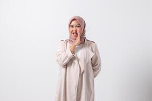 Portrait of excited Asian hijab woman in casual suit screaming announcement and whispering gossip. Businesswoman concept. Isolated image on white background photo