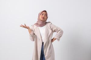 Portrait of confused Asian hijab woman in casual suit spreading hands sideways, feeling doubt while making choice. Businesswoman concept. Isolated image on white background photo