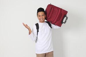 Portrait of excited Asian muslim man carrying suitcase pointing with hand to the side. Going home for Eid Mubarak. Isolated image on white background photo