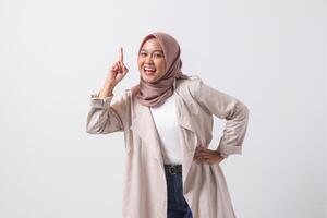 Portrait of excited Asian hijab woman in casual suit pointing up her forefinger and reminding something to do. Businesswoman concept. Isolated image on white background photo