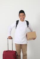 retrato de alegre asiático musulmán hombre que lleva maleta y cartulina caja mientras preparando para el vuelo. yendo hogar para eid mubarak. aislado imagen en blanco antecedentes foto