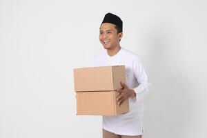 Portrait of excited Asian muslim man in koko shirt with peci carrying cardboard box. Going home for Eid Mubarak. Isolated image on white background photo
