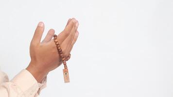 Close up hand of religious Asian muslim man in koko shirt with skullcap praying earnestly with his hands raised, holding islamic beads. Devout faith concept. Isolated image on white background photo