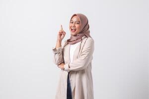 Portrait of excited Asian hijab woman in casual suit pointing up her forefinger and reminding something to do. Businesswoman concept. Isolated image on white background photo