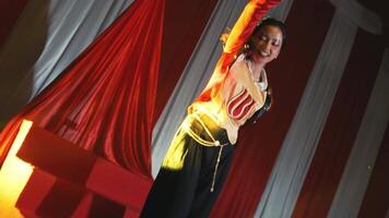 Performer in a red and black costume singing on stage with dramatic lighting and curtains in the background. video