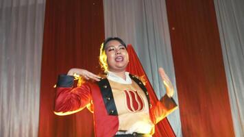 Female performer in vibrant costume singing on stage with dramatic lighting and red curtains in the background. video