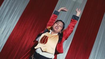 Excited young woman dancing with joy in a stylish red jacket against a striped background. video