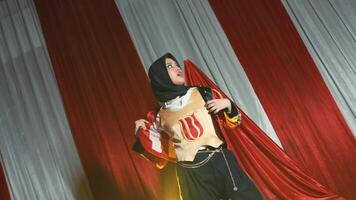 Confident woman in a superhero costume with a cape, posing against a striped background. video