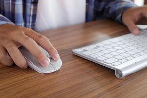 cerca arriba de masculino mano utilizando inalámbrico teclado y ratón en oficina escritorio. casual trabajando concepto foto