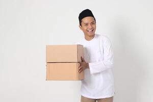 Portrait of excited Asian muslim man in koko shirt with peci carrying cardboard box. Going home for Eid Mubarak. Isolated image on white background photo