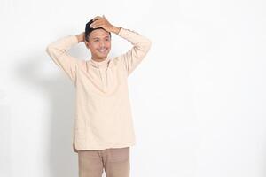 Portrait of excited Asian muslim man in koko shirt trying to adjust his songkok or peci or black skullcap. Isolated image on white background photo