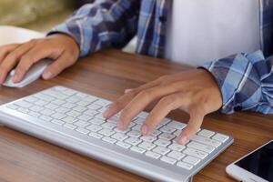 cerca arriba de masculino mano utilizando inalámbrico teclado y ratón en oficina escritorio. casual trabajando concepto foto