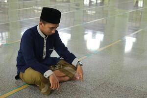 Portrait of religious Asian man in muslim shirt praying and doing salat or sholat in mosque photo