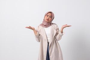 Portrait of confused Asian hijab woman in casual suit spreading hands sideways, feeling doubt while making choice. Businesswoman concept. Isolated image on white background photo