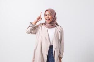 Portrait of excited Asian hijab woman in casual suit pointing up her forefinger and reminding something to do. Businesswoman concept. Isolated image on white background photo