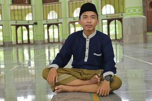 Portrait of religious Asian man in muslim shirt sitting in mosque photo