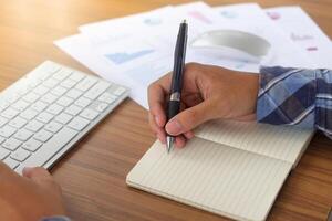 Close up of male freelance worker hand working on laptop and pointing with finger on analysis data with business graph and chart of information diagram on office desk in the morning photo