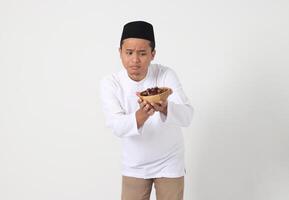 Portrait of excited Asian muslim man eating date fruit during sahur or breaking the fast. Culture and tradition on Ramadan month. Isolated image on white background photo
