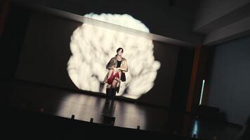 ejecutante en etapa con dinámica Encendiendo y proyección de un cerebro en el fondo, exhibiendo un creativo presentación o jugar. video