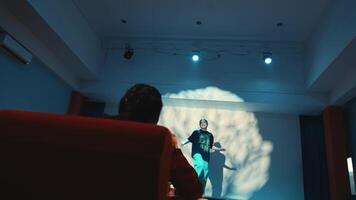 Speaker presenting at a conference with a projection screen in the background, audience in foreground. video