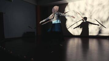 Silhouette of a young girl dancing with a hoop, casting a large shadow on a wall in a dimly lit room. video