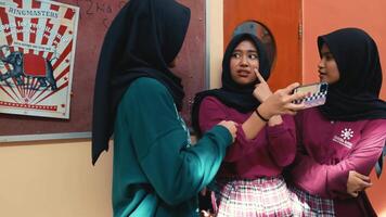 drei jung Frauen im Hijabs beschäftigt, verlobt im ein lebhaft Konversation in der Nähe von ein Bekanntmachung Tafel. video
