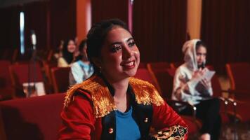 sonriente mujer disfrutando un espectáculo en un teatro con audiencia en el antecedentes. video