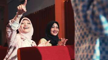 Two women in hijabs laughing and clapping hands in a festive setting with warm lighting. video