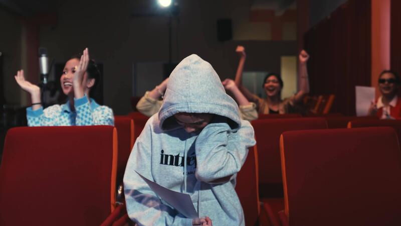 Embarrassed person hiding face with hoodie in a theater while others laugh around them