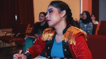 Focused woman in a stylish jacket sitting at a conference table with a pen and smartphone, with blurred audience in background. video