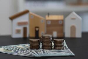 Real Estate Investment and Savings Concept. Cash and coin stacks in front of wooden house models symbolizing real estate investment. photo