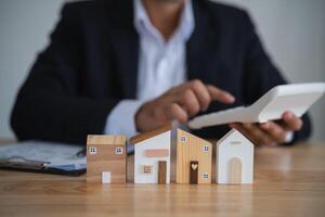 Professional Evaluating Wooden House Models. Businessperson with calculator analyzing wooden house models, concept of real estate evaluation. Finance home loan or interest concept. photo