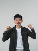 Cheerful Teen Boy with Braces Celebrating Victory. Joyful Asian teen boy with braces clenching fists in a triumphant gesture on a grey background. Portrait handsome man in studio concept. photo