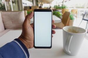 joven hombre mano utilizando inteligente teléfono con vacío pantalla a café foto