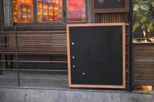 Empty wooden blackboard mockup standing outdoors in front of cafe photo