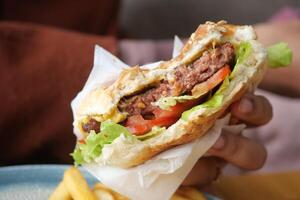 Mano sujetando hamburguesa de ternera en la mesa de cerca foto