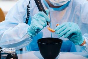 A masked and gloved dental technician works on a prosthetic tooth in his lab photo