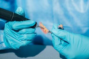 un enmascarado y enguantado dental técnico trabajos en un protésico diente en su laboratorio foto