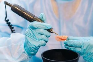 un enmascarado y enguantado dental técnico trabajos en un protésico diente en su laboratorio foto