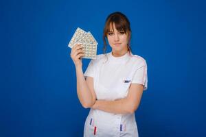 The concept of health care. A young brunette doctor in a white coat on a blue background shows plates with capsules to take. photo