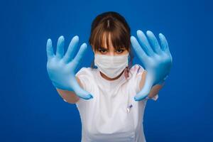 A girl doctor stands in a medical mask and gloves on an isolated blue background photo