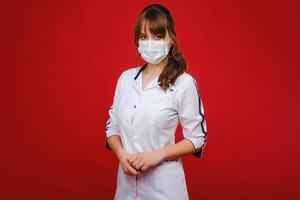 A female doctor stands in a medical mask isolated on a red background. photo