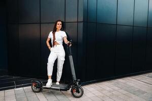 beautiful girl in white stylish clothes on an electric scooter in the city photo