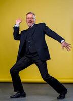 Senior manager man dancing at funny pose with expression. Yellow background. photo