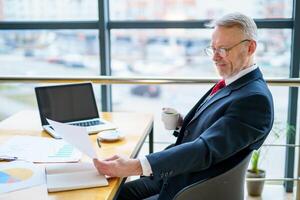 Thoughtful middle aged businessman in suit with a laptop on table while working with documents. photo