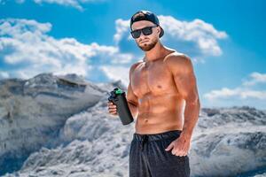 Portrait of a handsome halfnacked bodybuilder man. Glasses and a cap on. Sport bottle of water in hands. photo