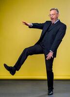 Senior manager man dancing at funny pose with expression. Yellow background. photo