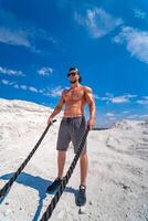 fuerte carrocero en un gorra y Gafas de sol formación con cuerdas exterior. pesado formación en un cantera. blanco paisaje. foto