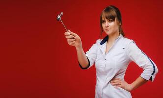 A doctor in a white coat holds a neurological hammer on a red background to test reflexes photo