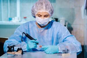 un dental técnico en protector ropa es trabajando en un protésico diente en su laboratorio foto